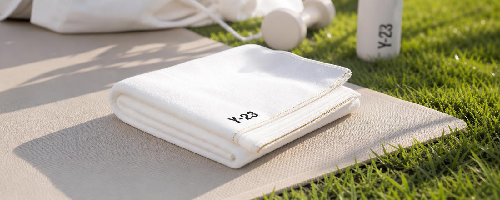 Premium Y-23 activewear towel folded on a yoga mat in a bright, clean outdoor setting